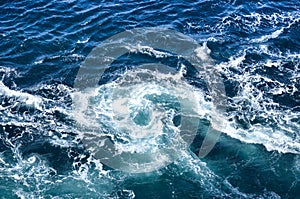 Abstract background. The waves of the sea water meet with underwater pointed rocks, forming whirlpools.