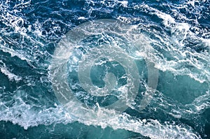 Abstract background. The waves of the sea water meet with underwater pointed rocks, forming whirlpools.