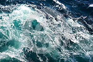 Abstract background. The waves of the sea water meet with underwater pointed rocks, forming whirlpools.