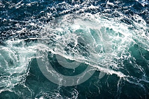 Abstract background. The waves of the sea water meet with underwater pointed rocks, forming whirlpools.