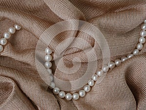 Abstract beige knitted fabric background. Soft pink shiny fabric. Delicate rose textile texture with pearls. Folds