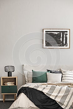 Black oil painting in frame on empty beige wall of cozy bedroom