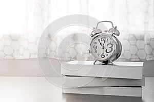 Abstract Black and White image of alarm clock put on stack of books on wooden table.