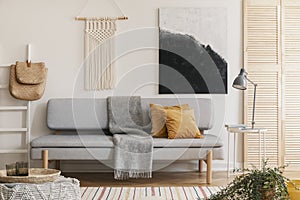 Abstract black and white painting and handmade macrame on white wall of natural living room interior with grey fashionable couch