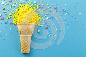Abstract blue background with wafer cone and yellow cake topping sprinkles scattered - top view photo with copy space