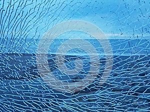 Abstract blue broken glass with a lot of cracks shot window against sea beach background