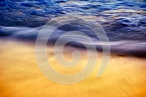 Abstract blue and golden silky ocean waves crashing on shore.