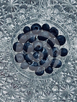 Abstract blue-tinged overhead shot of blueberries at the centre of an ornate crystal dish.