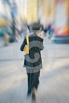 Abstract blurred background in motion of girl in black clothes and hat on city street, rear view. Selective soft focus