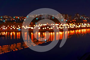 Abstract blurred bokeh of city, neon night lights, illumination, various colors in night with reflection in the lake. City life in
