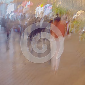 Abstract blurred image of unrecognizable silhouettes of people walking in city street in evening, shopping. Urban modern