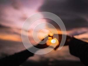 Abstract Blurred Photo of Silhouette Heart Hand sign with Sunrise