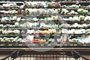 Abstract blurred photo of Supermarket aisle with empty shopping cart  in department store. Fruits and vegetables on shelves
