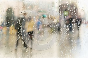 Abstract blurred silhouettes of people with umbrellas on rainy day in city, two persons seen through raindrops on window