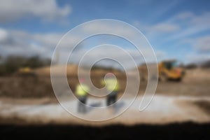 Abstract blurred workers in high vis jackets and hard hats on a construction site with dumper digger truck