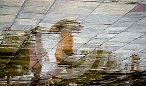 Abstract blurry silhouette reflections of unrecognizable people walking under umbrella on wet city street pavement on a rainy day