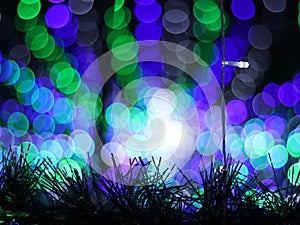 Abstract Bokeh light blurred background, lightbulb on Christmas tree for celebrate season with green, blue and purple colorful.
