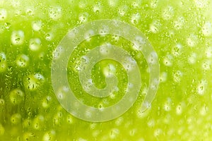 Abstract, bright green background in raindrops behind wet glass