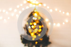 Abstract christmas tree. Blurred image of christmas tree made of pine branches with golden festive lights hanging on white wall.