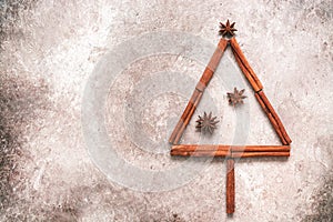 Abstract Christmas tree made of cinnamon sticks and star anise on a beige grunge background. Top view, flat lay. Noel