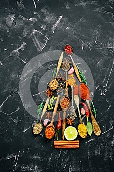 Abstract Christmas tree made of spices and seasoning in spoons. Black stone background. Top view, flat lay, vertical