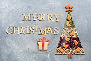 Abstract Christmas tree made from various legumes and almonds decorated with slices of mandarin on a gray background. The concept