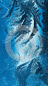 Abstract Christmas vertical background. Blue tinted phone wallpaper. Ice crystals on frozen window glass. Frost drawing. Winter