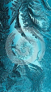 Abstract Christmas vertical background. Blue tinted phone wallpaper. Ice crystals on frozen window glass. Frost drawing. Winter