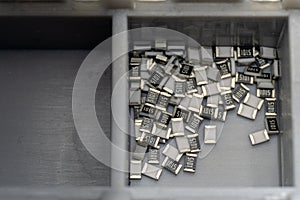 Grey scattered microscopic SMT surface mount chip resistors sorted in grey storage container photo