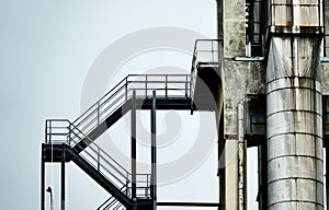 Abstract colourless picture of an iron staircase next to an aluminium pipe at the tower of an industrial plant