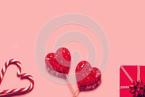 Abstract composition with two decorative hearts, lollipops and red present box on pink paper background