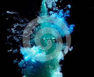 Abstract concept of teal color ink drop plume in water on an isolated  black background with bubbles