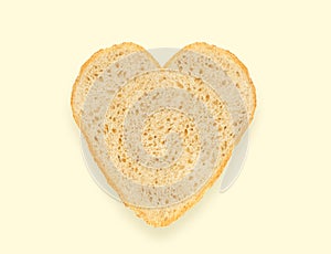 Abstract creative heart shaped cut-out from slice of white bread on light yellow background. Minimal flat lay