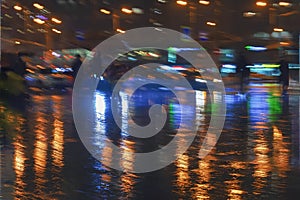 Abstract dark background of modern city at rayny night, bright illumination, reflection on wet asphalt, blurred