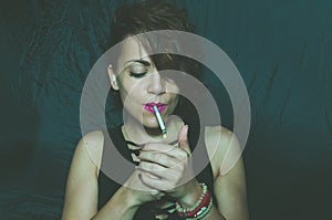 Abstract dark portrait of beautiful young girl with messy hair holding and lightning cigarette.