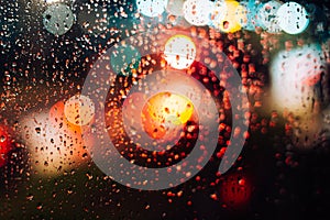 Abstract defocus background, night city lights through wet glass with rain drops, bokeh effect