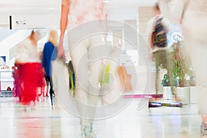 Abstract defocused motion blurred young people walking in the shopping center. Beautiful figure of a girl with shopping