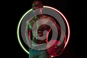 Abstract desing. Young african man, muscular athletewith basketball ball isolated on black background with neon