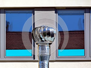 Abstract elevation view of stainless steel rotating exhaust vent in front of blue windows.