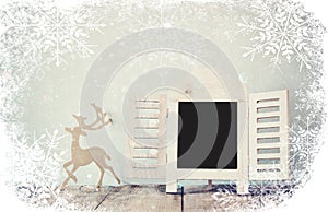 Abstract filtered photo of decorative chalkboard frame and wooden deer over wooden table. ready for text or mockup with snowflakes