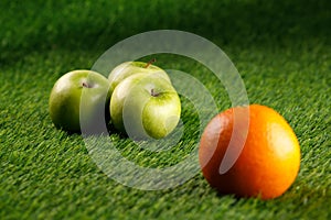 Abstract green background. Bush grass. Copy space. Three green apples and one orange.Close-up