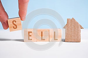 Abstract house made of cardboard hand holds with wooden cubes with the word sell. Home sale concept