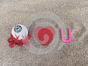 Abstract I love you with an eye ball a heart shape and the letter U on beach sand