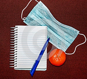 Abstract image with medical mask, tangerine, pen and notepad with blank lettering