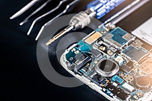 The abstract image of the smartphone`s motherboard and tools laying on table and black copy space is backdrop.