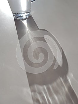 Abstract image of sunlight shining through glass of water, creating a clear ray of light and shadow, hydration theme