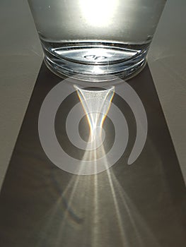 Abstract image of sunlight shining through glass of water, creating a clear ray of light and shadow, hydration theme