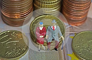 Abstract isolated figures of a retired old couple sitting on a stack of euro coins money - pension and retirement savings concept