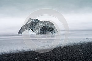 An abstract large piece of glacier ice sits on a black sand beach in Iceland