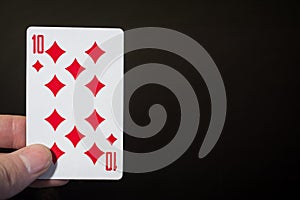 Abstract: man hand holding playing card Ten of Diamonds isolated on black background with copyspace